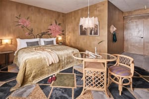 A luxurious bedroom with metallic fabric bedding, gold accents, and a stylish chair with a glass table.