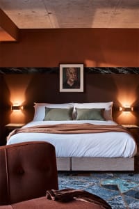 A modern bedroom featuring a bed with green accent pillows and a fabric headboard against a brown and black marble accent wal