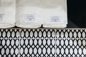 Three white towels with 'PEANUTS HOTEL' labels rolled up and placed on a shelf above a wall with black and white patterned ti