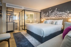 Modern bedroom featuring a neatly made bed with white linen, a comfortable seating area, and a stylish bathroom in the backgr