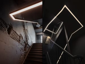 Modern, industrial-style staircase with black metal railing illuminated by linear, geometric lighting fixtures against a blac