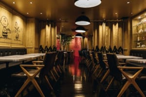 A dimly lit cafe interior with dark wooden tables and chairs, white walls, and red signage.