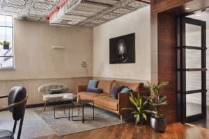 A modern coffee shop lounge area with a concrete and wood theme, featuring a brown leather couch, a coffee table, and potted 
