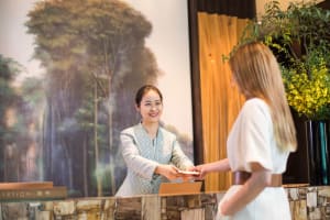 A hotel reception desk featuring a natural stone surface with a smiling receptionist interacting with a guest.
