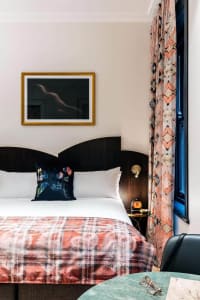 A mid-century modern bedroom with a bed featuring a plaid blanket, white pillows, and wooden headboard, patterned curtains, a