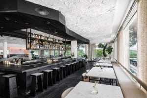 Modern cafe bar with white concrete precast walls and ceiling, featuring a well-lit bar area with stools and a long table for