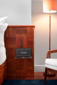 A bedroom featuring a wood-paneled wall with a Marshall speaker placed on a wooden nightstand.