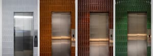 Four elevator doors framed by multicolored tiles with metal panels