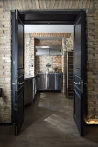 Industrial-style kitchen with brick walls, steel cabinets, and wooden flooring.