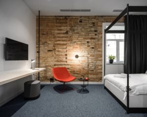 A minimalist bedroom featuring a red chair, a modern bed, and a brick wall.