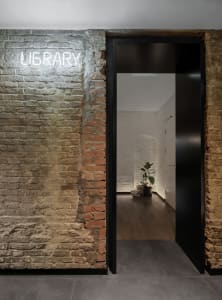 A modern library entrance featuring brick walls, concrete flooring, hardwood floors, and a black door with a neon sign readin