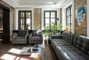 Modern living room with grey furniture, brick walls, and green plants.