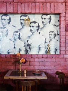 A restaurant interior with a pink brick wall featuring a poster of men in suits with flowers in their hair.