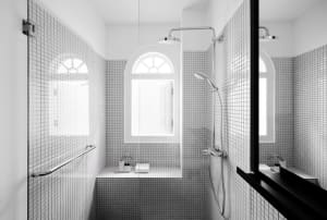 Modern bathroom with white tiled walls, glass shower enclosure, and arched windows.