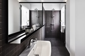 Modern minimalist bathroom featuring black and gray square tiles, a sleek white sink, and a walk-in shower with a rain shower