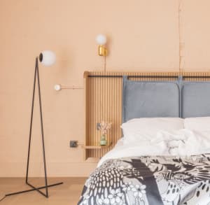 A modern minimalist bedroom featuring a wood headboard, a grey upholstered bed, and a white floor lamp with a round white glo