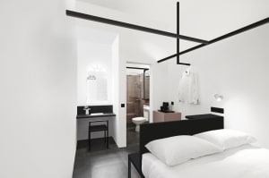 Modern minimalist bedroom with white walls, black furniture, and white bedding.