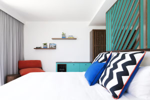 A modern bedroom with a white bed, black and white zigzag throw pillows, and blue accent cushions.