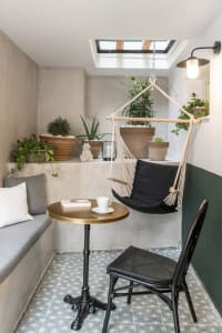 Industrial-style living room with concrete walls, a black hammock chair, and various potted plants.