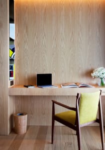 A minimalist home office workstation with a wooden desk, yellow upholstered chair, and light wood paneling.