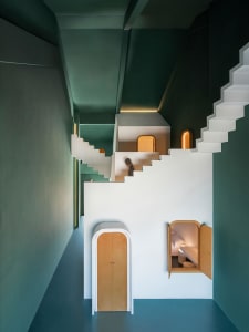 Modern residential interior with vibrant green walls, white and green stairs, and a cozy alcove bedroom.