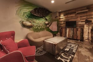 A cozy industrial-style living room with a retro trunk as a centerpiece, wooden panel walls, and a mural of a fishing boat on