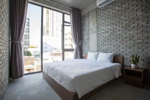 Modern minimalist bedroom with a bed, white bedding, grey curtains, and a brick wall