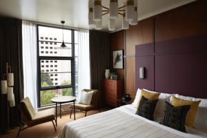 A modern hotel room featuring wooden paneling, fabric bedding, and metal accents.