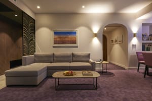 A modern living room featuring a light-colored sofa with a chaise lounge, centered around a table with fresh fruit and a book