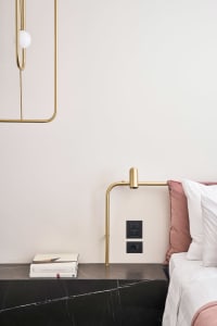 A modern bedroom with a marble headboard, brass accents, and neutral color palette.