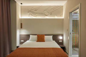 A modern minimalistic bedroom with a white bed and orange bedding and decorative wall features.