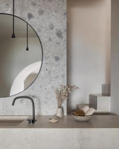 Modern minimalist bathroom featuring a circular mirror mounted on a terrazzo wall, a floating vanity, and dried flowers in a 
