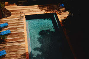 A modern outdoor wooden pool deck with clear water and blue lattice chairs.