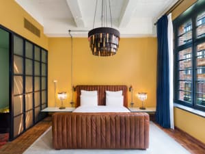 A minimalistic bedroom featuring a brown leather upholstered bed with white sheets, placed against a yellow wall beneath a ro