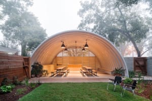 Outdoor space with a wooden, domed structure, featuring seating arrangements under a roof.
