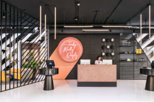A modern lobby featuring concrete walls and floors, with a reception desk and neon sign