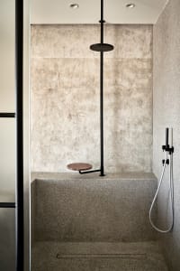 Minimalist bathroom with a stone shower featuring a concrete seat and a modern showerhead mounted on the wall.