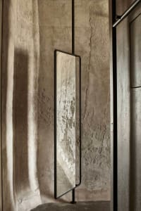 A minimalist interior design featuring metal-framed floor-to-ceiling mirror with a concrete wall backdrop.