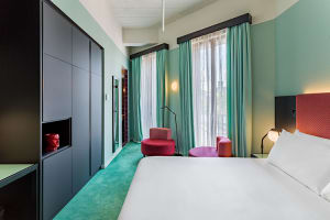 A modern hotel room with green carpet, turquoise curtains, and concrete flooring.
