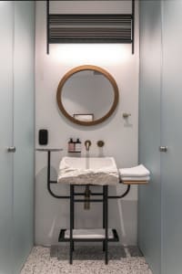 A minimalist bathroom featuring a concrete sink and mirror with a round wooden frame, and a towel rack mounted on the wall.