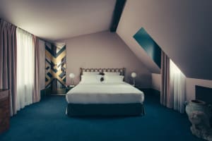 Modern minimalist bedroom with textured white walls and a bed adorned with a white bedspread and pillows. Room features simpl