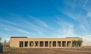 A minimalist vacation resort with a flat roof and arched openings in the desert, featuring sand-colored walls and a clear blu