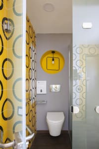 A contemporary bathroom with yellow patterned tiles, a white toilet, and a circular light fixture.
