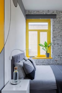 A bedroom featuring a bed with a grey headboard and grey, black, and white pillows, next to a bedside table with a glass and 