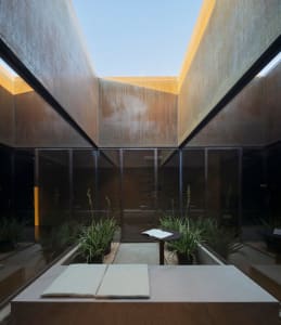 A modern interior space with concrete walls and glass walls, featuring a central table with cushions and an open book.