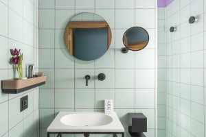 Bathroom with green and white tiled walls featuring a sink, mirror, and purple accents.