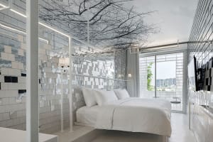 A modern minimalist bedroom featuring mirrored metallic tiles on the walls and ceiling, creating a reflective and spacious en