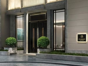 Modern hotel lobby entrance featuring concrete columns, glass doors, and potted green plants.