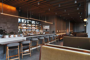 A modern restaurant bar interior featuring wooden walls, leather seating, and concrete flooring.