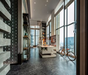 Modern, minimalist living space with concrete walls and floor, featuring a bicycle in the foreground and large windows offeri